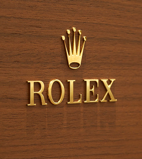 Logo da Rolex dourado em parede marrom com detalhes de madeira