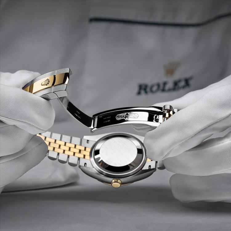 Homem com luvas brancas mostrando fecho da pulseira aberto com trava do relógio Rolex prata com detalhes ao centro em dourado